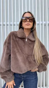 Chaqueta de piel sintética en color chocolate, con cuello clásico, cierre frontal metálico y bolsillos laterales. Presenta un diseño de corte holgado con ruedo ajustable mediante elástico.