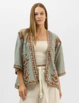Cardigan tipo kimono de color verde con bordados florales en tono marrón a lo largo de los bordes frontales y en las mangas. Presenta un corte amplio y fluido con mangas tres cuartos.