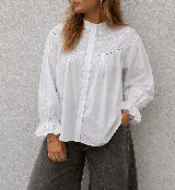 Camisa blanca de algodón con detalles de bordado inglés y calados en el canesú. Presenta cuello alto, cierre frontal de botones y mangas largas con puños terminados en volados bordados.