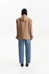 Tapado corto tipo blazer confeccionado en lana de color tostado. Presenta una capucha integrada, cierre frontal con dos botones negros y bolsillos laterales con solapa.