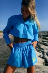 Short de poplín de algodón color azul vibrante, con cintura elástica ancha, bolsillos laterales y estampa de logo en color amarillo neón en el lateral izquierdo.