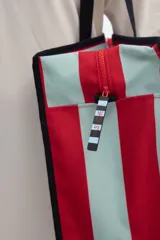 Cartera tote bag con diseño de rayas verticales en negro y blanco, asas de hombro y ribetes en color celeste. Cuenta con cierre superior y estampa con el nombre de la marca.