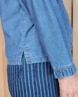 Camisa de denim con cuello alto tipo mao con volados, cierre frontal con botones y mangas largas con puños elásticos con volados.