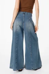 Jean de corte wide leg con pinzas frontales y costuras verticales decorativas. Presenta un diseño de tiro alto con cierre de botón y cremallera, confeccionado en denim de lavado medio.
