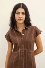 Vestido corto camisero de jean azul oscuro con cuello clásico, cierre frontal con botones y mangas cortas. Presenta costuras decorativas en color blanco.
