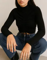 Sweater de cuello alto y manga larga, confeccionado en tejido de punto acanalado. Presenta un diseño ajustado al cuerpo con un detalle de fruncido central ajustable mediante cordones en la parte frontal.