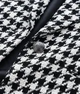 Blazer de sastrería confeccionado en tejido tweed con estampado pied de poule en blanco y negro. Presenta cuello con solapa, cierre frontal con un botón, mangas largas y bolsillos frontales con solapa.