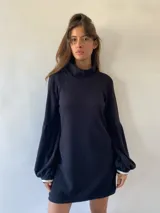 Vestido corto de tejido tipo waffle en color negro, con cuello alto, mangas largas abullonadas y puños con detalle de tejido en contraste blanco.