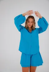 Conjunto de dos piezas confeccionado en lino color blanco. Incluye una camisa de corte holgado con mangas abullonadas y bolsillos frontales, y un short de tiro alto con cintura elástica y forro interior.