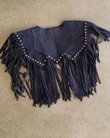 Chaleco corto de cuero azul marino, estilo western, con cuello solapa y profusión de flecos largos en todo el contorno. Presenta detalles de tachas metálicas plateadas a lo largo del borde del cuello y los hombros.