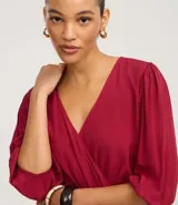 Blusa color vino tinto, con escote cruzado en V, mangas tres cuartos abullonadas con elástico en el puño y peplum ajustado en la cintura con lazo regulable.