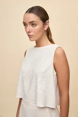 Top sin mangas color blanco con escote redondo, calce amplio y diseño con bordado floral en relieve.