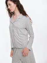 Camisa de pijama de manga larga con cuello solapa y cierre frontal de botones. Presenta un estampado sutil de pequeños corazones sobre una base de color gris melange, con detalles de ribete en contraste en el cuello y la botonera.