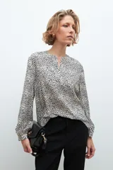 Blusa beige con estampado de lunares negros, cuello en V y mangas largas.
