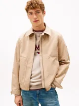 Campera Tommy Hilfiger modelo Ivy, color beige, confeccionada en tejido técnico impermeable y resistente al viento. Cuenta con cuello clásico, cierre frontal de cremallera, bolsillos laterales ribeteados y parche engomado en la manga.
