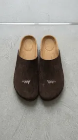 Zueco estilo sandalia de diseño cerrado, color beige, confeccionado en material texturizado con plantilla anatómica y suela plana. Presenta el logotipo de la marca grabado en la parte frontal.