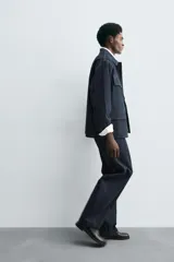 Pantalón de corte barrel fit confeccionado en denim de algodón rígido color azul oscuro. Presenta cintura con pliegues frontales, bolsillos laterales y bolsillos traseros de vivo. Cierre frontal con cremallera y gancho metálico oculto.