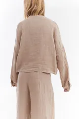 Camisa blanca de lino italiano, de corte holgado, mangas largas abullonadas, cuello mao y cierre frontal con botones, con diseño para anudar en la cintura.