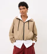 Campera cortaviento Marfinno de color beige, diseño corto con capucha, cierre frontal de cremallera con tiradores negros, bolsillos laterales y elástico fruncido en el ruedo y los puños.