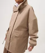 Campera cortaviento oversized color beige, de cuello alto, mangas largas con puños elásticos, bolsillos frontales con solapa y cordón ajustable en la cintura.