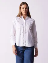 Camisa blanca de algodón con cuello clásico, escote en V y cierre frontal con botones. Presenta apliques de brillos plateados en el frente y mangas largas con puños abotonados.