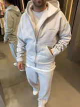 Campera con capucha y cierre frontal, confeccionada en tejido de punto gris jaspeado. Presenta un corte holgado, bolsillos tipo canguro y detalle de logo bordado en el pecho.