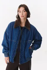 Campera de denim azul con corte oversized, cierre frontal y cuello de piel sintética marrón desmontable. Presenta detalles de volados en el frente, puños elásticos y logo bordado en el pecho.