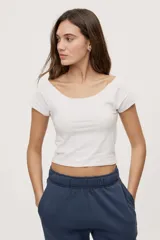 Remera blanca de corte ajustado y largo cropped, con escote redondo amplio y mangas cortas.