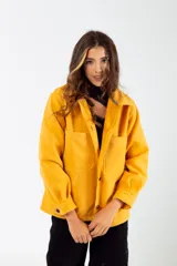 Camisa color mostaza de paño, corte oversize, con cuello clásico, cierre frontal con botones, mangas largas con puños abotonados y dos bolsillos de parche en el pecho.