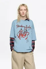 Remera de corte oversize color celeste con cuello redondo y mangas cortas. Presenta un estampado frontal con el logo de la marca y un dibujo de zapatillas de ballet en color rojo.