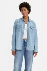 Camisa de jean estilo western, color azul claro, con cierre frontal de botones a presión, bolsillos en el pecho con solapa y costuras características del estilo vaquero.