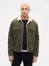 Campera de pana color verde oliva con interior y cuello de corderito sintético. Presenta cierre frontal con botones metálicos, bolsillos en el pecho con solapa y botones, y puños ajustables.