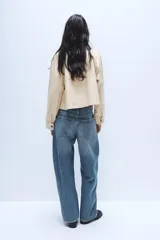 Jeans de tiro medio con diseño baggy barrel, confeccionados en denim color beige con efecto lavado. Presentan cinco bolsillos, costuras laterales torcidas y cierre frontal con cremallera y botón metálico.