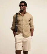 Bermuda masculina slim confeccionada en sarga de algodón con elastano, color beige, con bolsillos laterales tipo chino, bolsillos traseros embutidos con botón, trabillas en la cintura y cierre frontal con botón y cremallera.