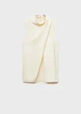 Blusa color crema de tejido fluido satinado, con cuello alto y diseño drapeado sin mangas. Cierre de botón en la parte posterior.