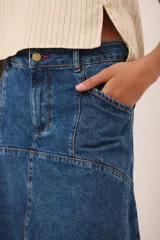 Falda midi de jean azul oscuro, con corte ligeramente acampanado y detalle de costura central vertical. Presenta paneles horizontales a la altura de la cadera que simulan bolsillos.