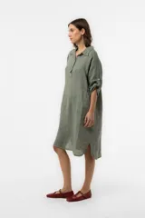 Vestido camisero midi de lino color beige, de calce relajado, con cuello clásico, cierre frontal parcial con botones, mangas 3/4 regulables y bolsillos delanteros.