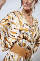 Vestido largo de corte fluido con estampado abstracto en tonos tierra, ocre y blanco. Presenta mangas tipo murciélago, escote en V profundo y un tajo frontal. Incluye un sistema de ajuste regulable en la cintura.