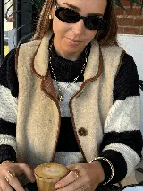 Chaleco de borrego color beige con ribetes de cuero marrón, cierre frontal de botones y cuello solapa. Es reversible.