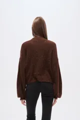 Polera de punto color marrón con destellos brillantes, cuello redondo, mangas largas abullonadas y diseño holgado.