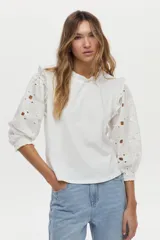 Blusa blanca con mangas abullonadas de broderie, cuello elevado con volados y detalles de volados en los hombros.