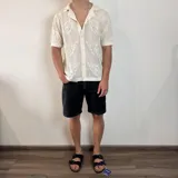 Camisa de tejido de punto calado color negro, con cuello solapa, cierre frontal de botones y mangas cortas.