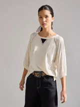 Remera de corte holgado en color crudo con sutiles rayas horizontales. Presenta mangas tres cuartos con puños elásticos, cuello redondo con detalle de costura en V y costuras decorativas oscuras en los hombros.
