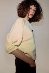 Chaqueta de punto color amarillo claro, con cuello redondo, mangas abullonadas por debajo del codo y cierre frontal con botones oscuros.
