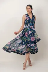 Vestido midi de organza azul marino con estampa floral en tonos rosados y verdes. Presenta escote en V cruzado con solapas, sin mangas, falda evasé de capas asimétricas y estructuradas.