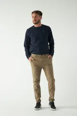 Pantalón chino color beige, de corte slim, con bolsillos laterales y traseros. Se ajusta a la cintura con cinturón de cuero marrón.