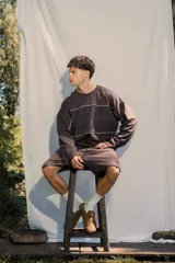 Buzo crewneck color chocolate, de tela rústica liviana, con estampado en el frente y la espalda. Presenta líneas blancas decorativas en el pecho y los brazos, y bordes deshilachados en los puños y el dobladillo.