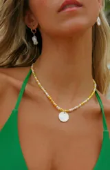 Gargantilla de cuentas en tonos amarillo, blanco y perlas, con un dije circular de nácar colgando al centro.
