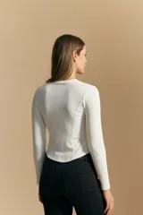 Remera blanca de manga larga con tejido acanalado, cuello redondo y corte ajustado al cuerpo. Presenta costuras verticales que definen la silueta.
