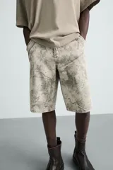 Bermuda relaxed fit de algodón, color beige con estampado abstracto en tonos grises. Cuenta con cinco bolsillos y cierre frontal de cremallera y botón.